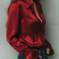 Uma elegante blusa de cetim cor de vinho com mangas largas e detalhes em renda 2025